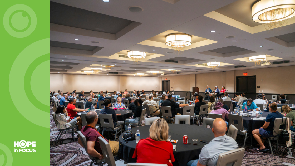 Attendees seated at round tables listening to speakers during a clinical trials information session