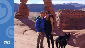 Michelle Ward Caton and her husband stand near Delicate Arch with her guide dog, Ryder