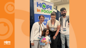 Four adults and a child stand smiling in front of a Hope in Focus display at a conference exhibit