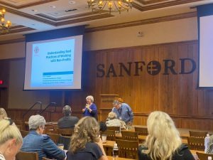 Two presenters speak to an audience in a conference room, with a presentation slide displayed